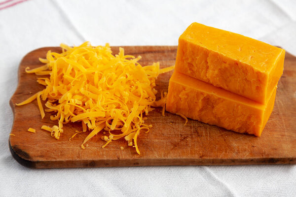 Shredded Sharp Cheddar Cheese on a rustic wooden board, side view. 