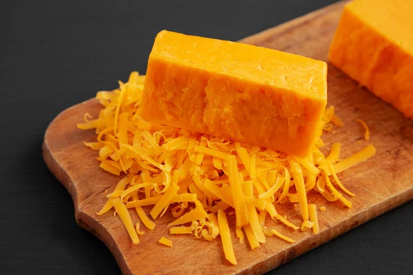 Siyah arka planda, ahşap bir tahtanın üzerinde doğranmış Çedar Peyniri.. 