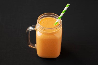 Ev yapımı Havuç Clementine Muz Smoothie. Siyah arka planda, cam kavanozda..