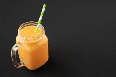 Siyah bir arka planda, cam kavanozda ev yapımı havuç Clementine Muzlu Smoothie. Boşluğu kopyala.