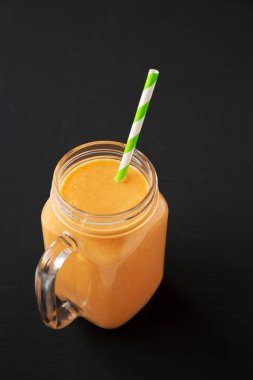 Ev yapımı Havuç Clementine Muz Smoothie siyah arka planda, düşük açılı cam kavanozda.