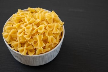 Siyah arka planda bir kasede çiğ organik Farfalle Makarnası. Metin için boşluk.