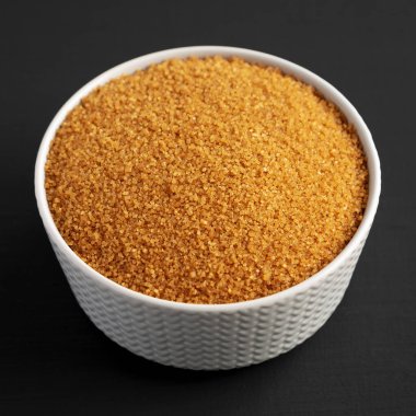 Kahverengi Demerara Şekeri siyah arka planda, düşük açılı bir kasede.