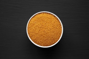 Kahverengi Demerara Şekeri, siyah bir yüzey üzerinde bir kasede, üst manzara. Dümdüz, tepeden, yukarıdan.