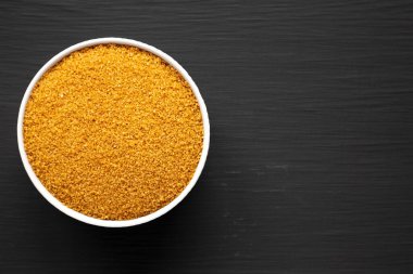 Kahverengi Demerara Şekeri, siyah bir yüzey üzerinde bir kasede, üst manzara. Dümdüz, tepeden, yukarıdan. Metin için boşluk.