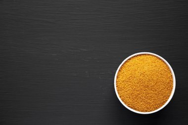 Kahverengi Demerara Şekeri, siyah bir yüzey üzerinde bir kasede, üst manzara. Dümdüz, tepeden, yukarıdan. Boşluğu kopyala.