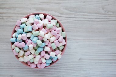 Beyaz ahşap bir arka planda pembe bir kasede Gökkuşağı Fruity Mini Marshmallowları, üst manzara. Dümdüz, tepeden, yukarıdan. Metin için boşluk.