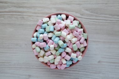 Beyaz ahşap bir arka planda pembe bir kasede Gökkuşağı Fruity Mini Marshmallowları, üst manzara. Dümdüz, tepeden, yukarıdan. 