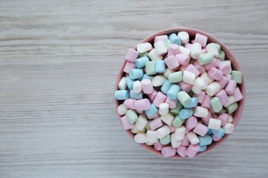 Beyaz ahşap bir arka planda pembe bir kasede Gökkuşağı Fruity Mini Marshmallowları, üst manzara. Dümdüz, tepeden, yukarıdan. Boşluğu kopyala.