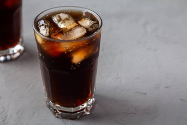 Soğuk serinletici Kola, gri yüzeyde, düşük açılı, buz küpleriyle. Metin için boşluk.