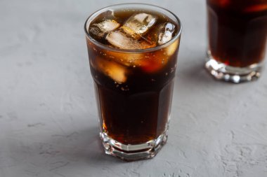 Buz küpleriyle soğuk serinletici Kola, gri yüzeyde pipet, düşük açı görünümü.