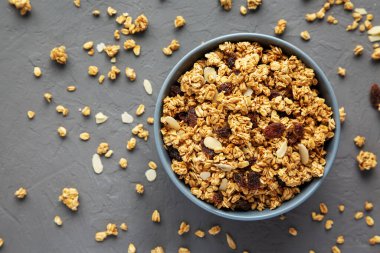 Gri bir yüzeyde kuru üzüm ve bademli ev yapımı granola. Dümdüz, tepeden, yukarıdan. 