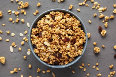 Gri bir yüzeyde kuru üzüm ve bademli ev yapımı granola. Dümdüz, tepeden, yukarıdan. 