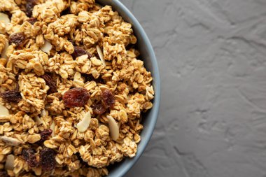 Gri arka planda, kuru üzüm ve bademli ev yapımı granola. Dümdüz, tepeden, yukarıdan. Boşluğu kopyala.