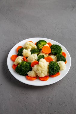 Gri bir yüzey üzerinde, havuç, brokoli ve karnabahar karışımı organik buharda pişirilmiş sebzeler.. 