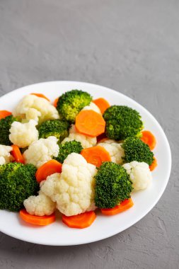 Gri bir yüzey üzerinde, havuç, brokoli ve karnabahar karışımı organik buharda pişirilmiş sebzeler. Boşluğu kopyala.