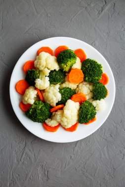 Gri bir yüzey üzerinde karışık organik buharda pişirilmiş sebzeler (Havuç, Brokoli ve Karnabahar). Dümdüz, tepeden, yukarıdan. 