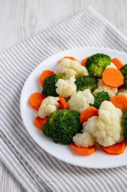 Beyaz ahşap bir zemin üzerinde, havuç, brokoli ve karnabahar karışımı organik buharda pişirilmiş sebzeler..