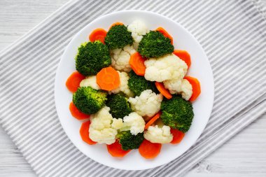 Beyaz ahşap bir zemin üzerinde, havuç, brokoli ve karnabahar gibi karışık organik sebzeler. Dümdüz, tepeden, yukarıdan.