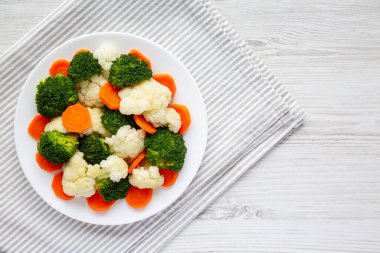 Beyaz ahşap bir zemin üzerinde, havuç, brokoli ve karnabahar gibi karışık organik sebzeler. Dümdüz, tepeden, yukarıdan. Metin için boşluk.