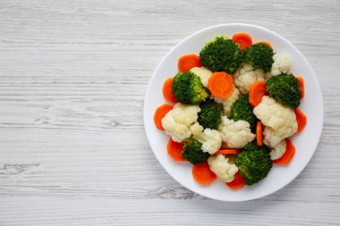 Beyaz ahşap bir zemin üzerinde, havuç, brokoli ve karnabahar gibi karışık organik sebzeler. Dümdüz, tepeden, yukarıdan. Boşluğu kopyala.