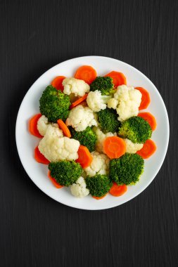 Siyah bir arka planda, havuç, brokoli ve karnabahar karışımı organik buharda pişirilmiş sebzeler. Dümdüz, tepeden, yukarıdan. 