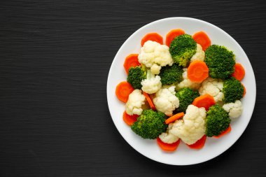 Siyah bir arka planda, havuç, brokoli ve karnabahar karışımı organik buharda pişirilmiş sebzeler. Dümdüz, tepeden, yukarıdan.