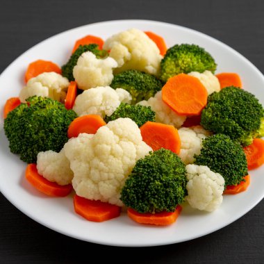 Siyah bir arka planda, havuç, brokoli ve karnabahar üzerine karışık organik buharda pişirilmiş sebzeler. Yakın plan..