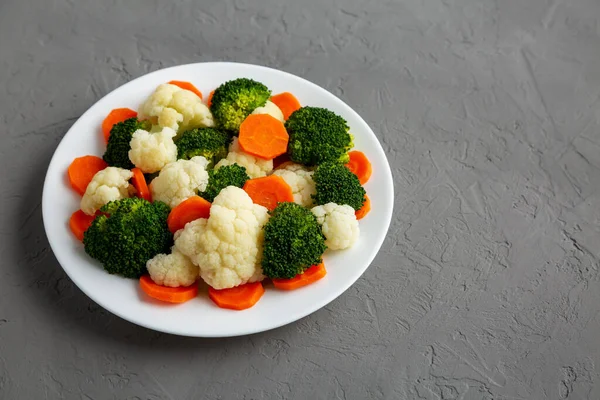 Gri bir yüzey üzerinde, havuç, brokoli ve karnabahar karışımı organik buharda pişirilmiş sebzeler. Boşluğu kopyala.