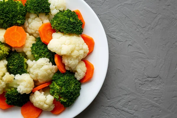 Gri arkaplanda bir plaka üzerinde karışık organik buharda pişirilmiş sebzeler (Havuç, Brokoli ve Karnabahar). Boşluğu kopyala.