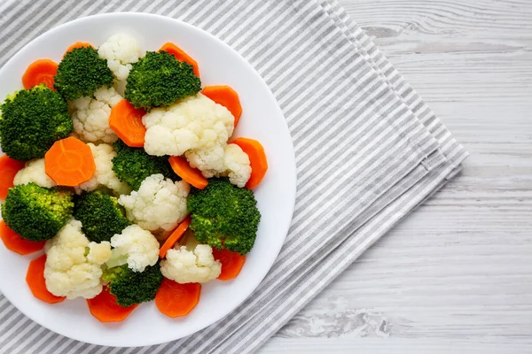 Beyaz ahşap bir zemin üzerinde, havuç, brokoli ve karnabahar gibi karışık organik sebzeler. Dümdüz, tepeden, yukarıdan. Boşluğu kopyala.