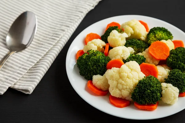 Siyah bir yüzey üzerinde, havuç, brokoli ve karnabahar karışımı organik buharda pişirilmiş sebzeler.. 