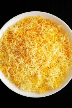 Siyah bir yüzey üzerinde, beyaz bir kasede doğranmış Meksika peyniri karışımı. Dümdüz, tepeden, yukarıdan. Yakın plan..