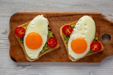 Beyaz ahşap bir yüzey üzerinde ev yapımı sağlıklı yumurta, avokado ve domates tostu. Dümdüz, tepeden, yukarıdan. 