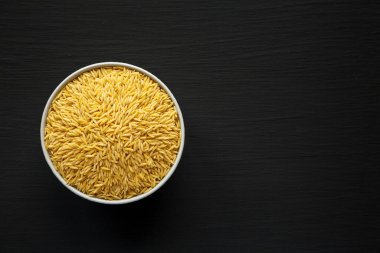 Siyah arkaplanlı çiğ organik risonili makarna. Dümdüz, tepeden, yukarıdan. Boşluğu kopyala.