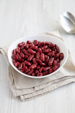 Kırmızı Organik Böbrek, beyaz ahşap bir yüzey üzerinde, beyaz bir kasede fasulye yiyor..