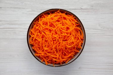 Beyaz ahşap arka planda bir kasede çiğ turuncu havuç parçacıkları, üst manzara. Yukarıdan, dümdüz uzanmış.