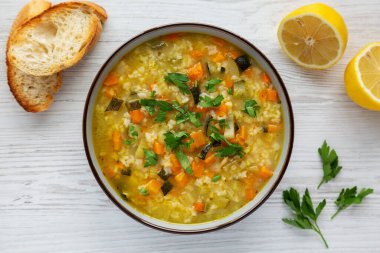 Homemade fresh lemon rice soup in a bowl on a white wooden surface, top view. Flat lay, overhead, from above. Copy space.