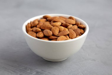 Raw brown almonds in a bowl on a gray background, low angle view. Close-up.