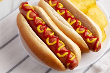 Homemade Hot Dog with Ketchup and Yellow Mustard with Chips on a Plate, side view. 