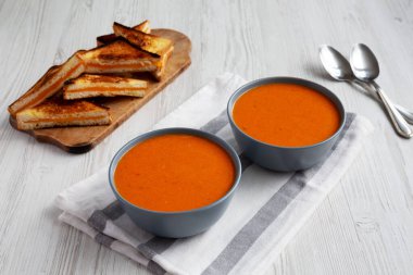 Homemade Tomato Soup with Grilled Cheese on a white wooden background, side view.