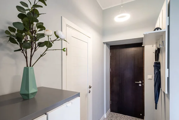 Interior ruang masuk abu-abu modern di apartemen. Umbrellas berpegangan pada gantungan putih. Bunga dalam vas. — Stok Foto