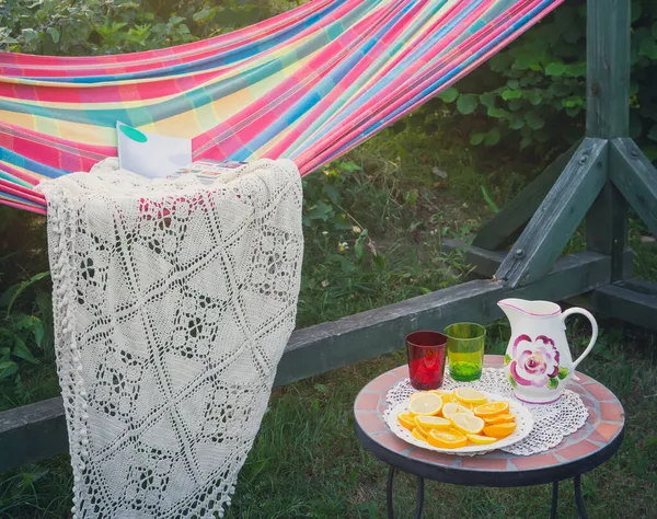 Hamaca en el jardín. Naranja, vasos y decantador en mesa pequeña. —  Fotos de Stock