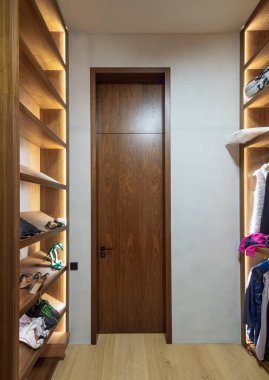 Lüks bir dairede modern bir soyunma odası. Ayakkabılar için aydınlatılmış raflar. Tahta kapı..