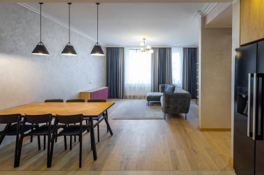 Lüks stüdyo dairede, aydınlık oturma odasının modern iç mekanı. Rahat gri bir kanepe. Boş raflar. Tahta masa ve siyah sandalyeler..