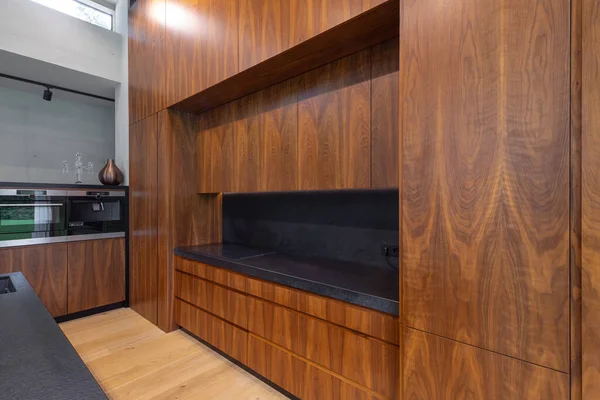 Siyah tezgahlı ahşap mutfağın modern iç mimarisi. Buil-in cihazları. Lüks daire. Işıklar açık..