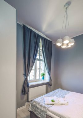 Yatak odasının gri tonlarında modern bir iç mekan. Pencere büyük boy yatağa karşı. Tavanda şık bir lamba.