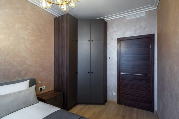 Modern interior of cozy bedroom in apartment. Brown colors. Pillow on bed. Wooden door.
