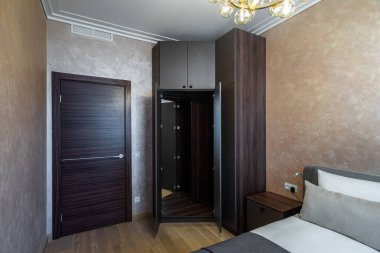 Modern interior of cozy bedroom in apartment. Brown colors. Pillow on bed. Wooden door.