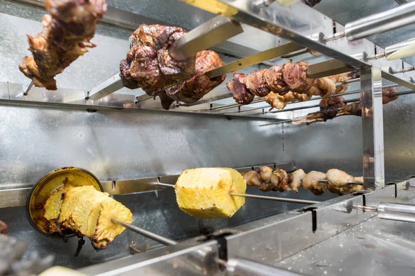 Pineapples and different meats are cooked on skewer on electric grill.